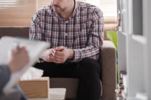 male patient sits and talks to a counselor with clipboard in a mood disorders treatment center