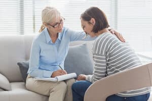 older female counselor takes notes as she comforts female patient during ocd treatment