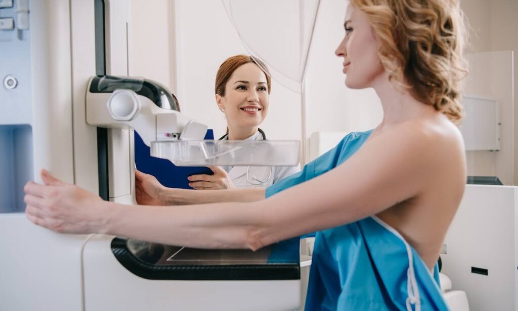 smiling radiologist standing near patient while making mammography diagnostics on x-ray machine